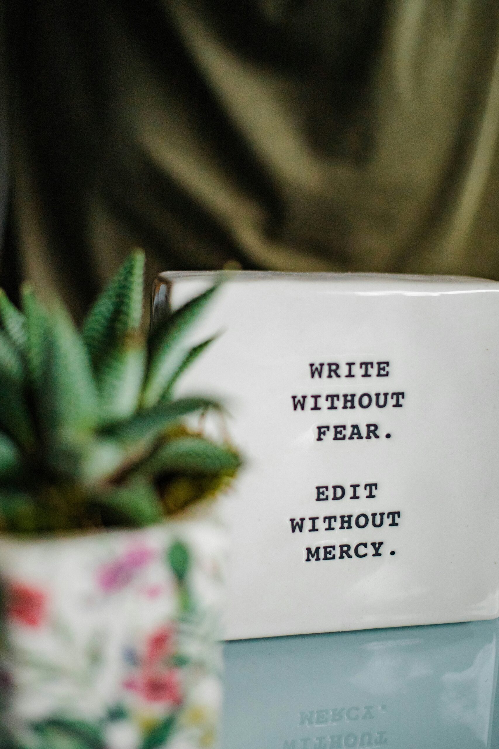 Eine Fliese mit der Aufschrift "Write without fear. Edit without mercy." steht neben einer Pflanze. Texterin Ines Kirschhock übernimmt Korrektorat und Lektorat für Sie.