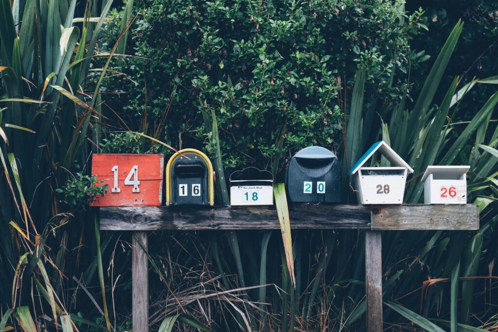 Briefkaesten_Newsletter_unsplash_mathyas-kurmann-fb7yNPbT0l8 Passend zum Thema Newsletter: Sechs bunte Briefkaesten vor gruenen Pflanzen.